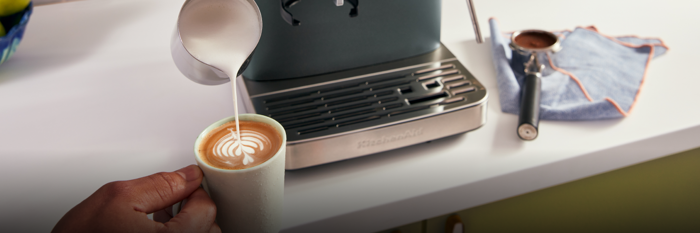 A person pouring steamed milk into a mug of espresso.