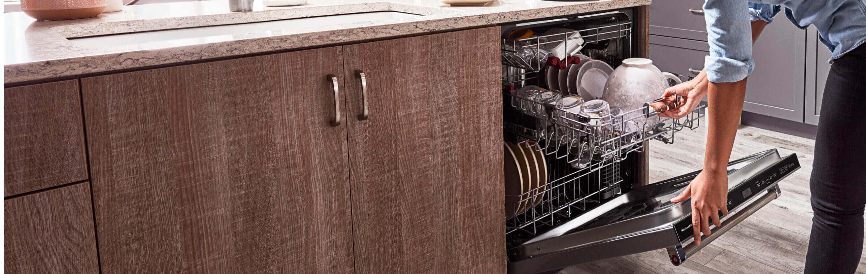 Hands opening a top control built-in dishwasher next to wood grain cabinets