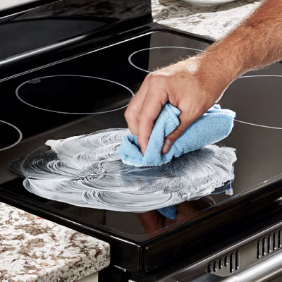 Hand wiping cleaner off an induction cooktop with a towel