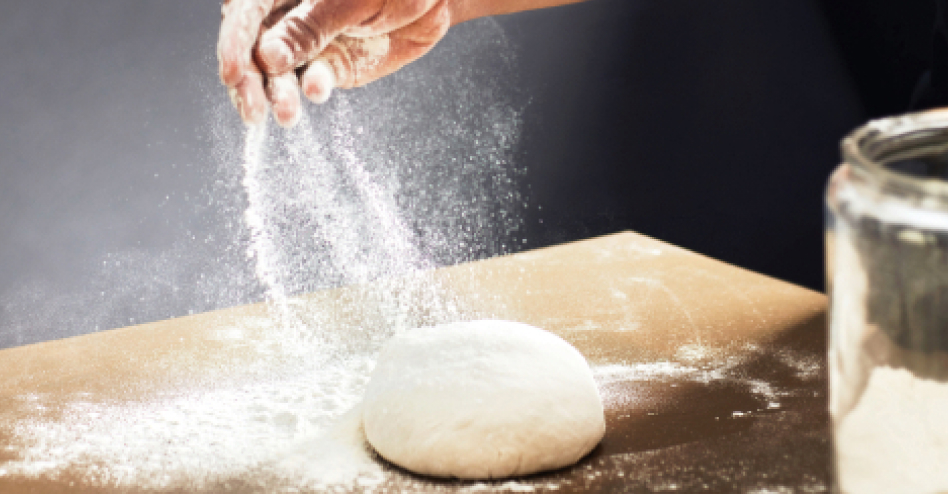 Hand sprinkling flour over a ball of dough Hand sprinkling flour over a ball of dough