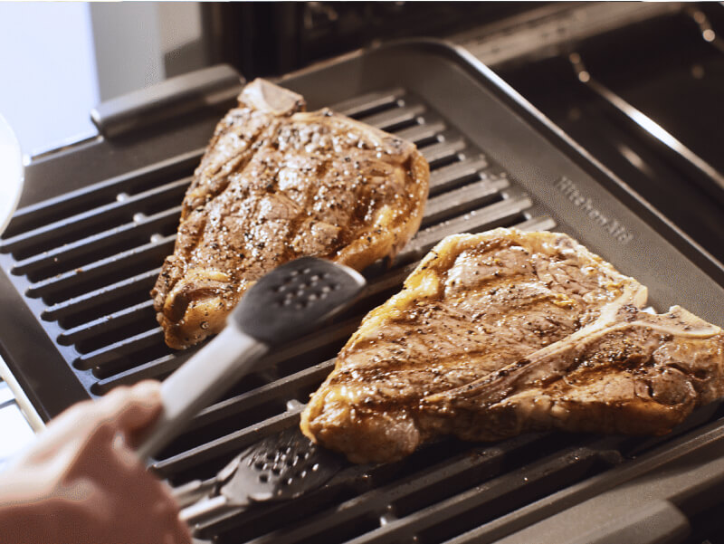 Person grilling a t-bone steak in their KitchenAid® smart oven