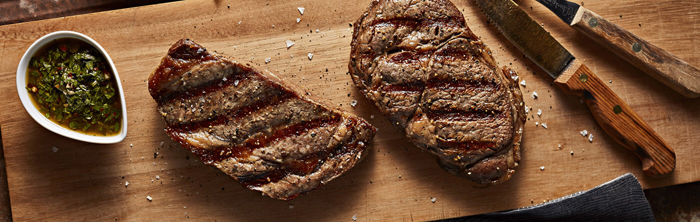 Steak resting on a cutting board next to a bowl of chimichurri sauce