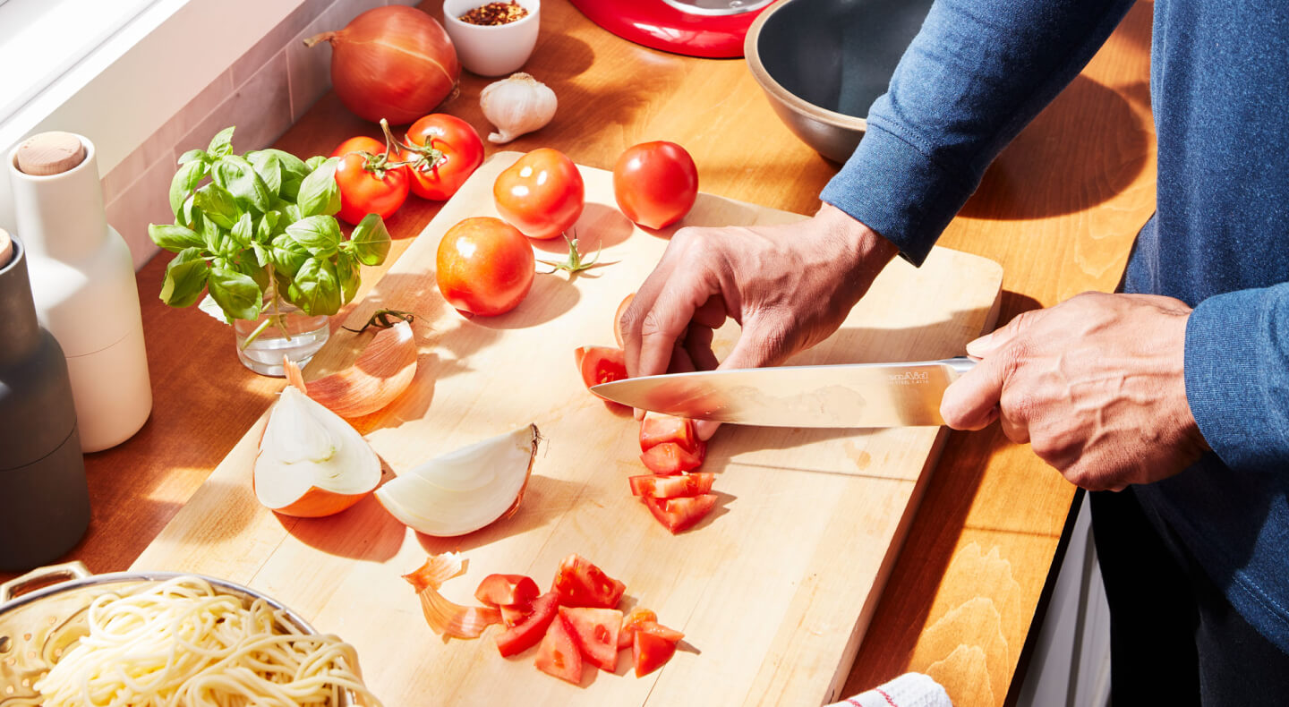A person chopping tomatoes on a cutting board A person chopping tomatoes on a cutting board
