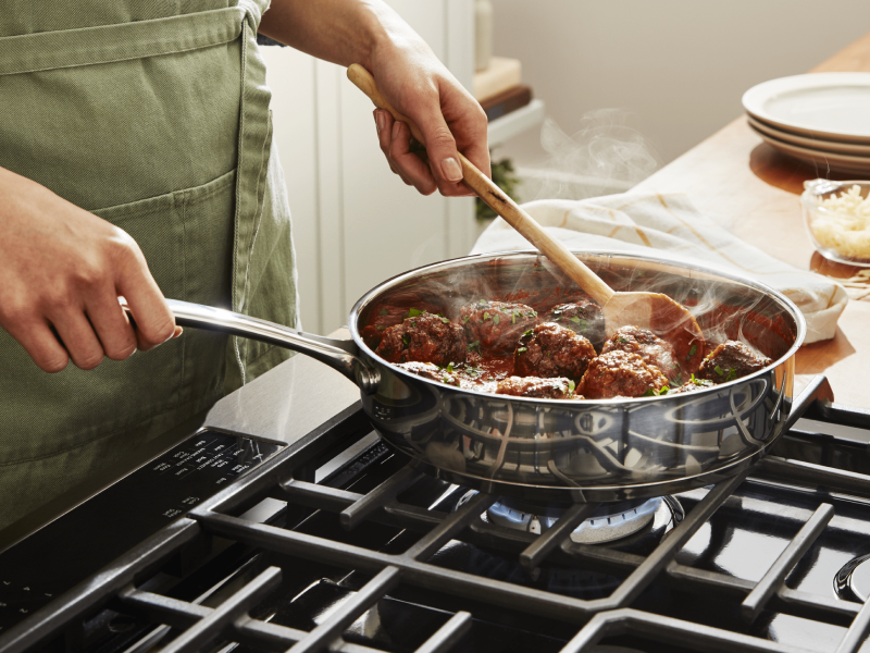 A person simmering vegan "meatballs" on a stovetop A person simmering vegan "meatballs" on a stovetop