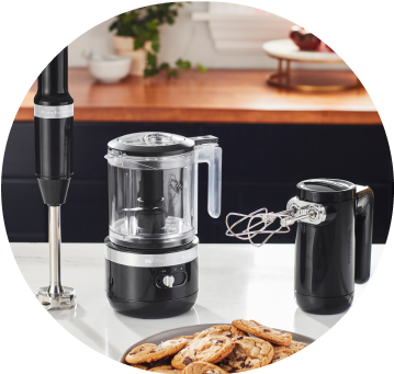 Matte Black KitchenAid® cordless immersion blender, food chopper, and hand mixer on white countertop.