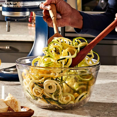 Woman tossing salad with veggie noodles in a glass salad bowl