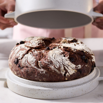 Maker uncovering top of bread bowl to reveal baked rye bread loaf