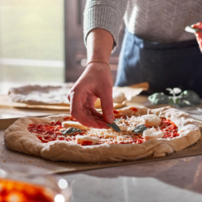 Person adding toppings to homemade pizza dough