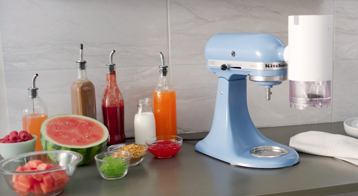 KitchenAid® stand mixer with shave ice attachment surrounded by syrups and fruit toppings KitchenAid® stand mixer with shave ice attachment surrounded by syrups and fruit toppings