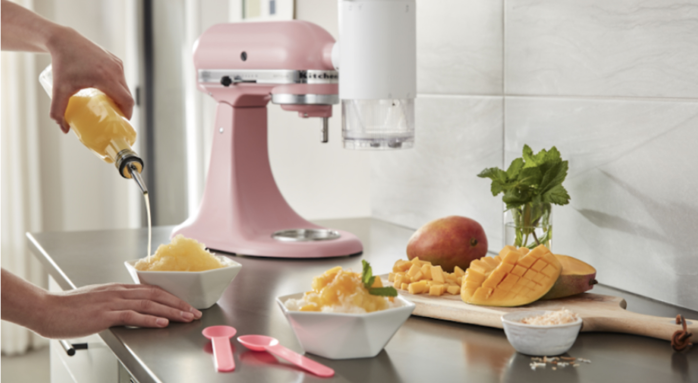 Person pouring syrup on a bowl of shaved ice surrounded by KitchenAid® stand mixer and chopped mangoes  Person pouring syrup on a bowl of shaved ice surrounded by KitchenAid® stand mixer and chopped mangoes
