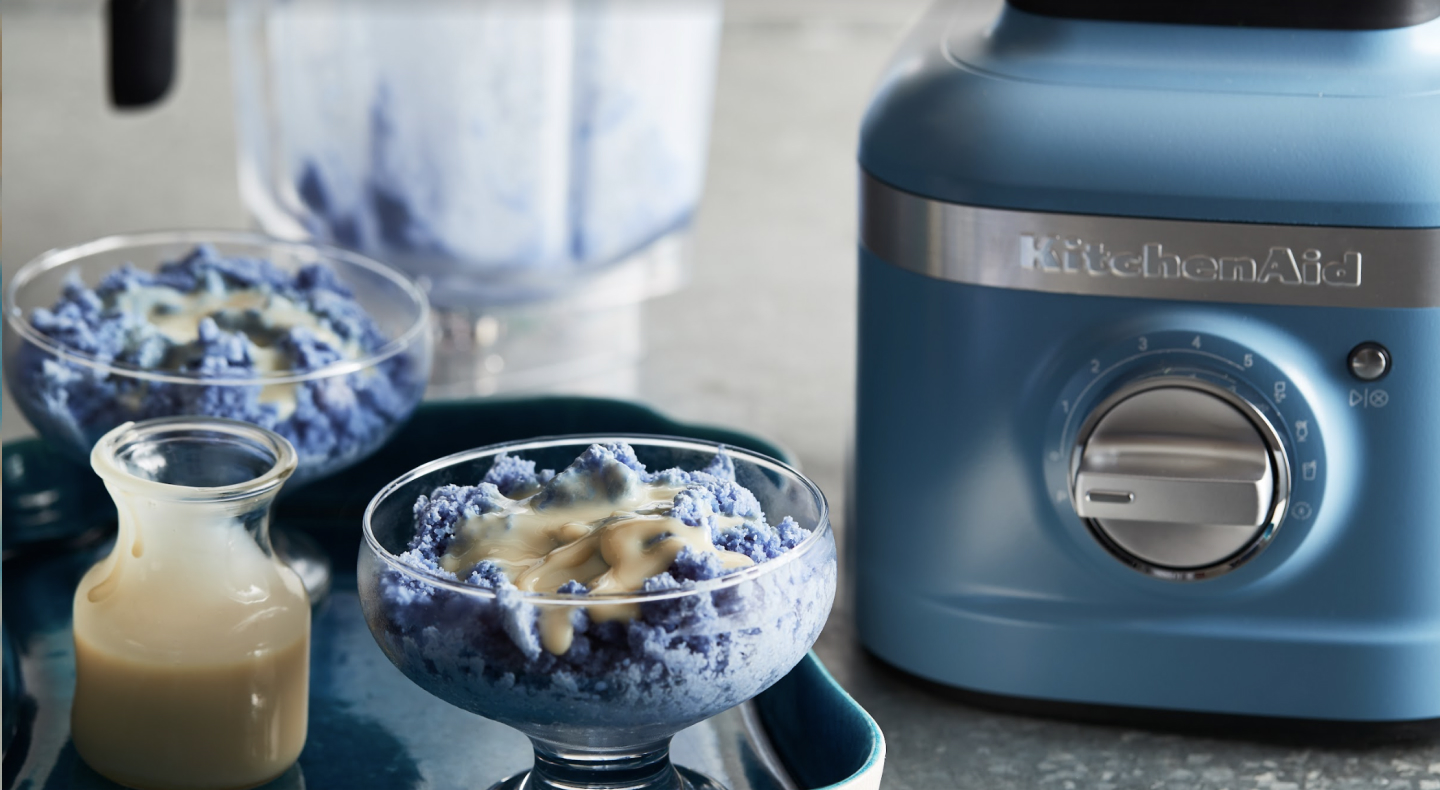 Blue baobing topped with condensed milk next to a KitchenAid® blender. Blue baobing topped with condensed milk next to a KitchenAid® blender.