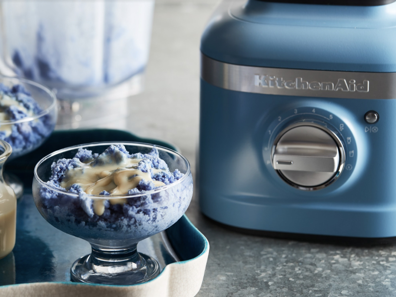 Blue baobing topped with condensed milk next to a KitchenAid® blender. Blue baobing topped with condensed milk next to a KitchenAid® blender.