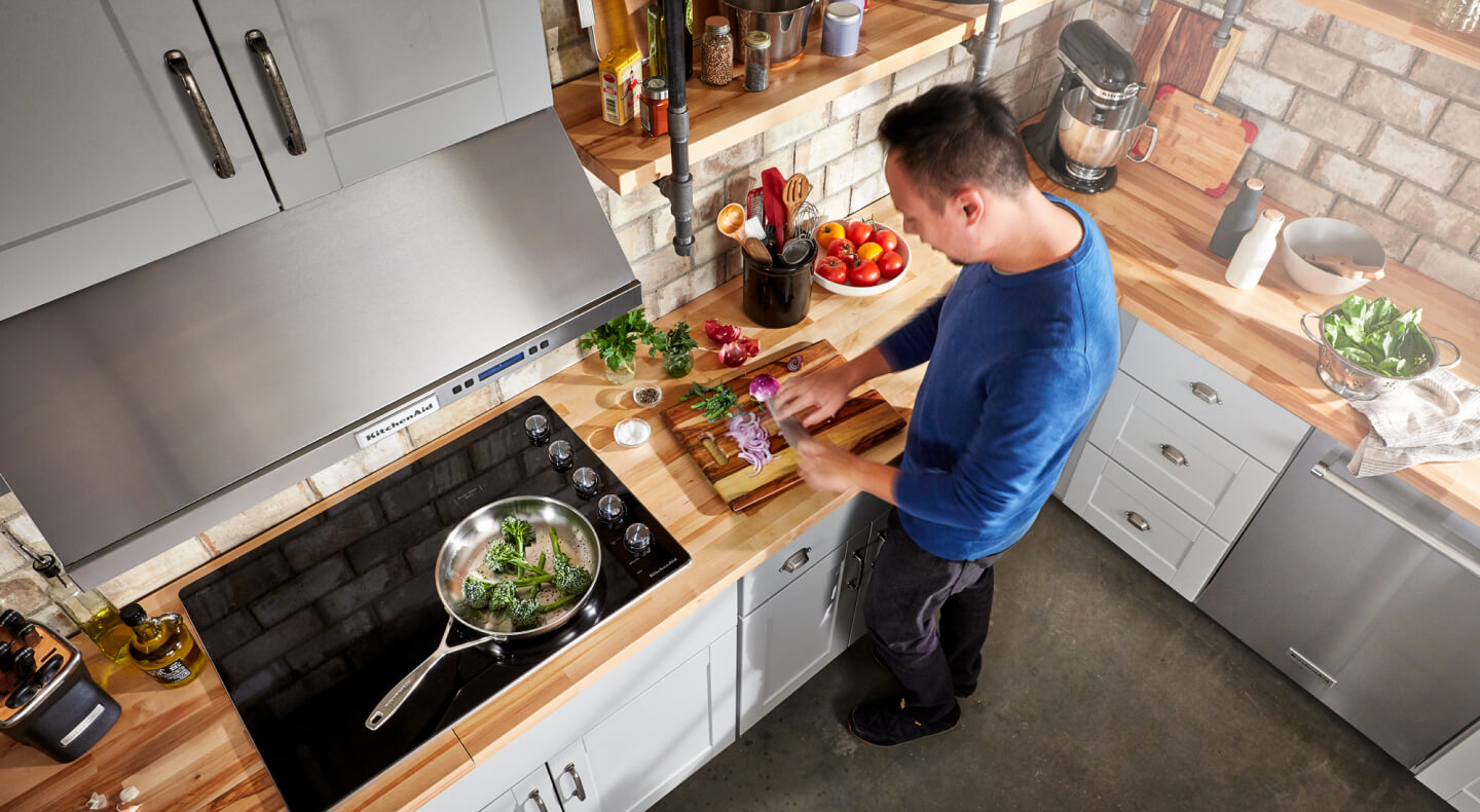 A person chopping vegetables next to their glass cooktop A person chopping vegetables next to their glass cooktop