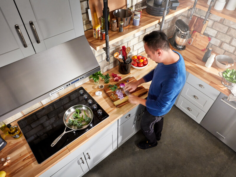 A person chopping vegetables next to their glass cooktop A person chopping vegetables next to their glass cooktop