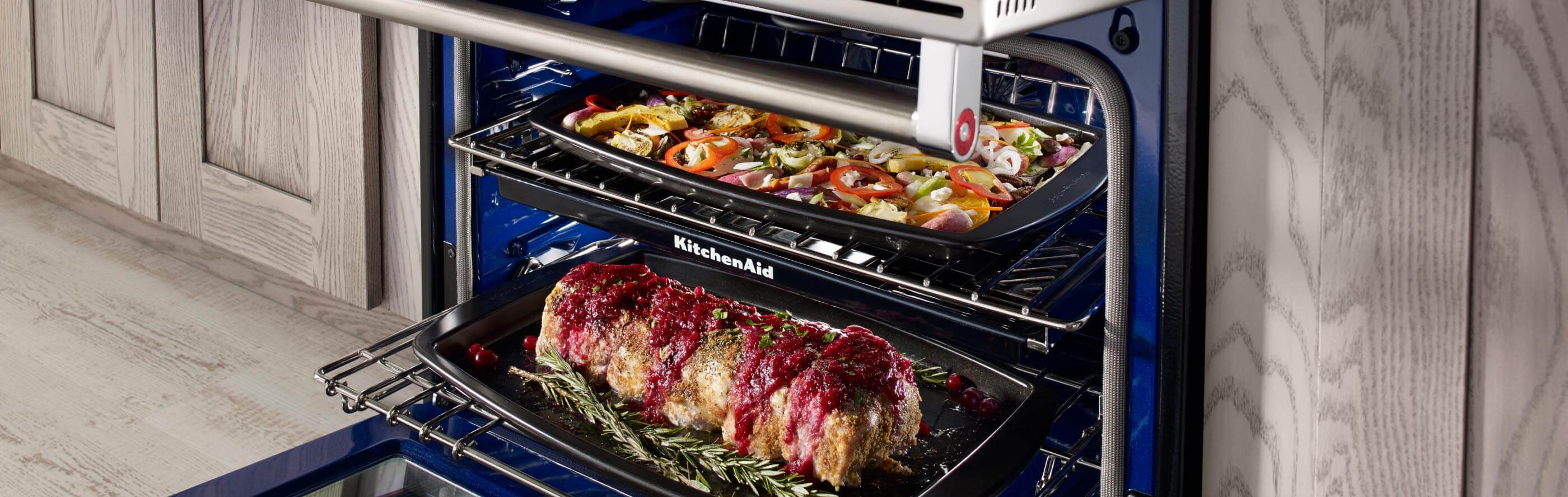 An open oven with a roast on the bottom rack and vegetables on the top rack