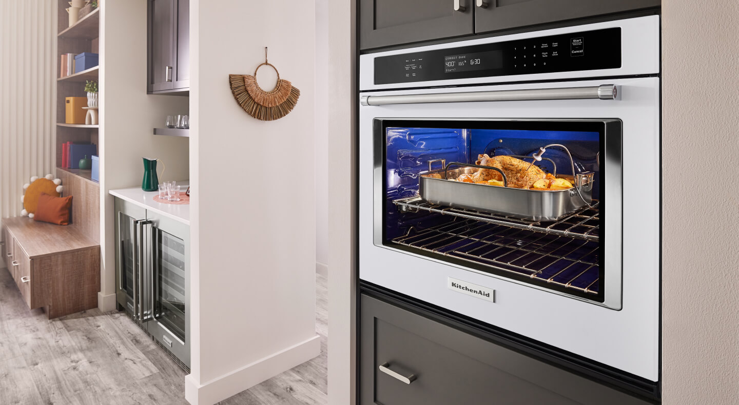 A pulled back image of a kitchen with an oven in it with a chicken roasting inside
