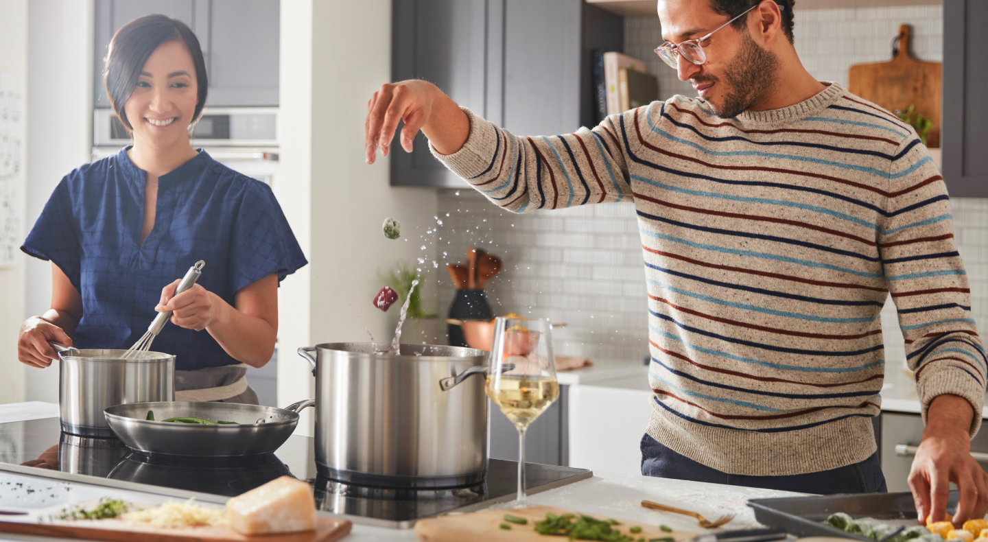 A man and woman preparing various dishes with a cooktop A man and woman preparing various dishes with a cooktop