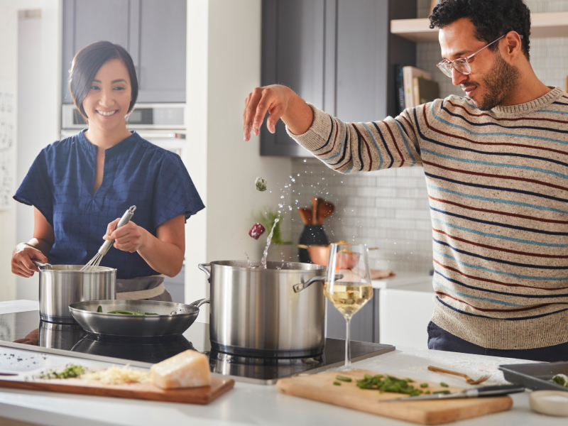 A man and woman preparing various dishes with a cooktop A man and woman preparing various dishes with a cooktop