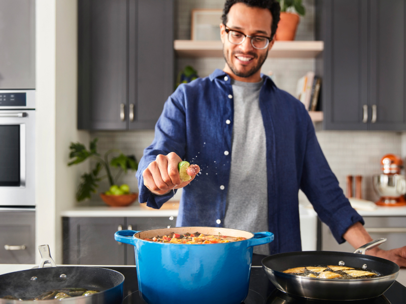 A man squeezing lime into a dish on a cooktop A man squeezing lime into a dish on a cooktop