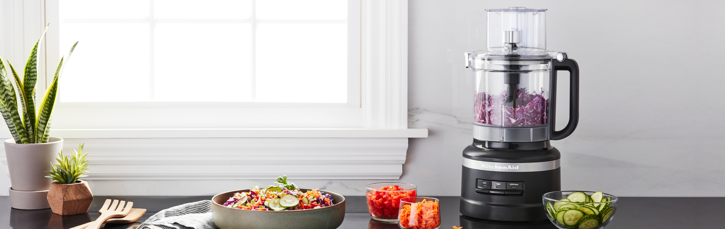KitchenAid® food processor on a counter among chopped and sliced vegetables.