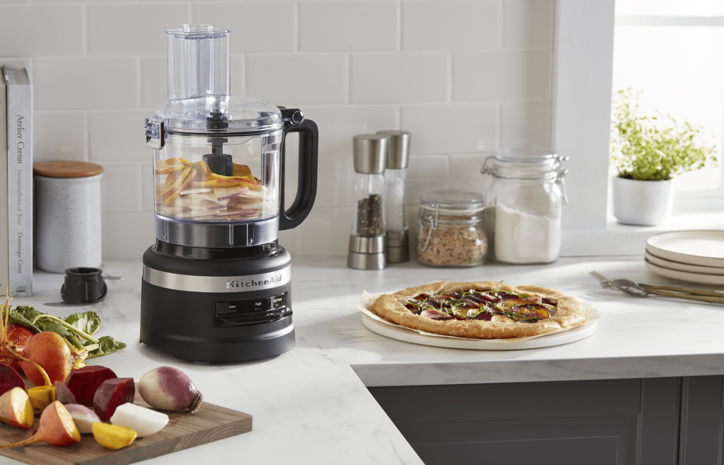 A black KitchenAid® food processor next to a pizza on the counter. A black KitchenAid® food processor next to a pizza on the counter.