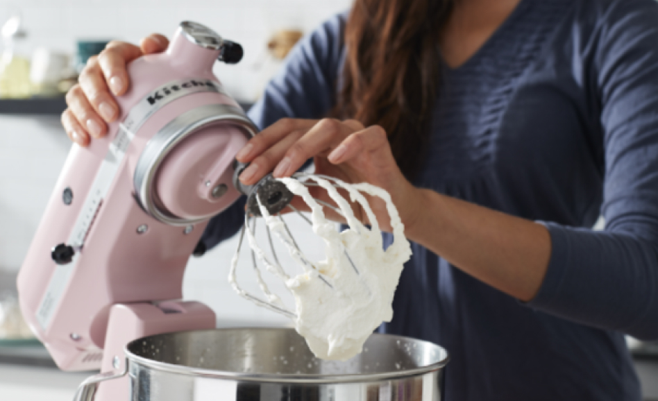 A woman removing the whip attachment from a pink stand mixer. A woman removing the whip attachment from a pink stand mixer.