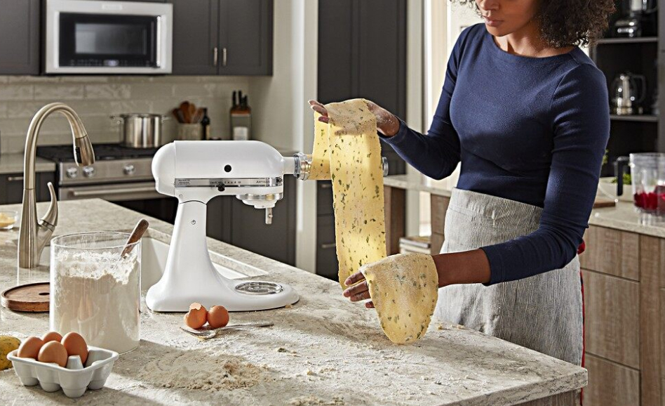Woman using white stand mixer to roll homemade pasta with an attachment Woman using white stand mixer to roll homemade pasta with an attachment