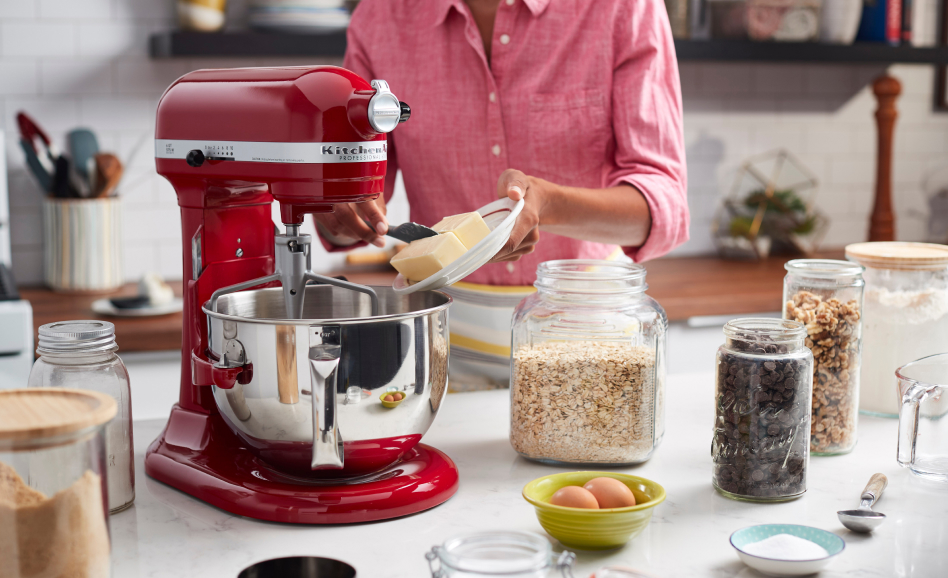 A red KitchenAid® stand mixer and a person adding butter to the bowl. A red KitchenAid® stand mixer and a person adding butter to the bowl.
