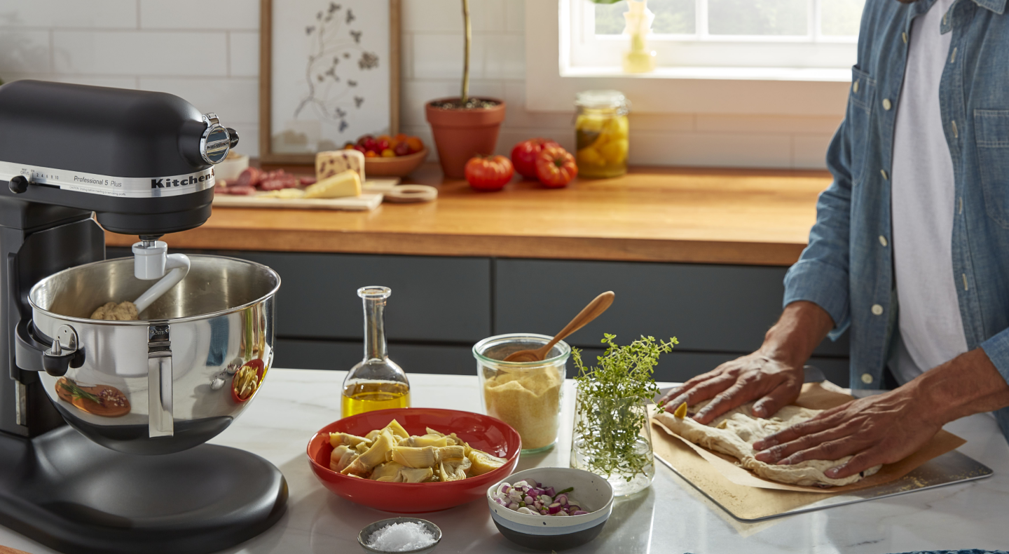 Person kneading dough on a countertop next to a matte black KitchenAid® stand mixer