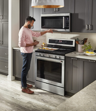 Person selecting settings on an over-the-range microwave above a gas range