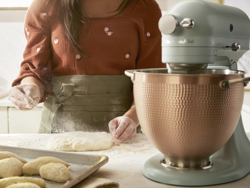 A person sprinkling dough with flour next to a KitchenAid® stand mixer. A person sprinkling dough with flour next to a KitchenAid® stand mixer.