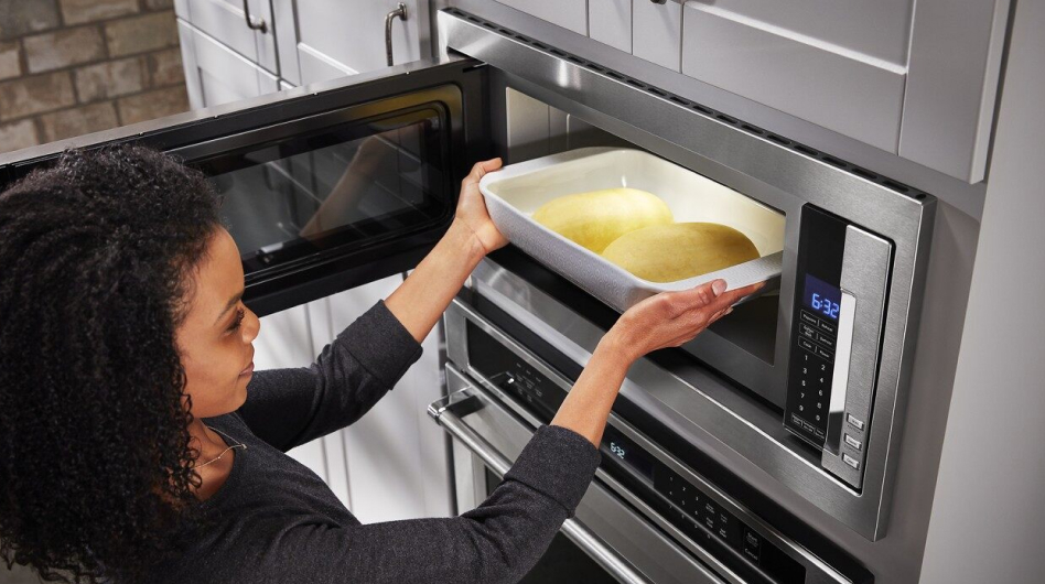Woman sliding casserole dish inside built-in microwave Woman sliding casserole dish inside built-in microwave