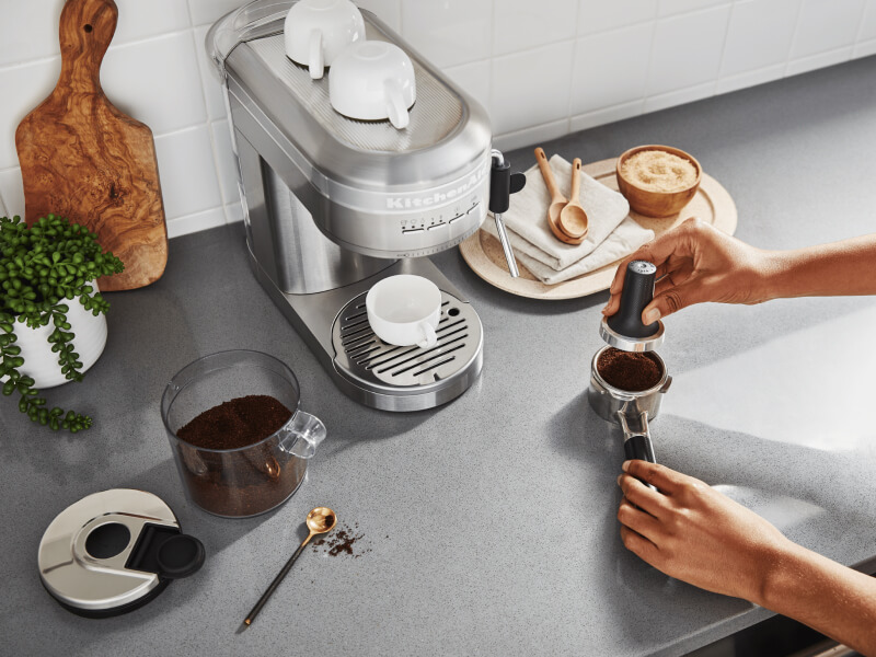 Person tamping espresso next to a KitchenAid® Semi-Automatic Espresso Machine