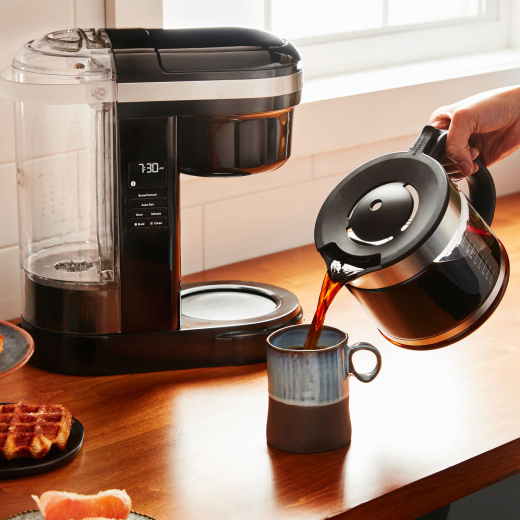 Person pouring coffee from a KitchenAid® Drip Coffee Maker into a ceramic mug Person pouring coffee from a KitchenAid® Drip Coffee Maker into a ceramic mug