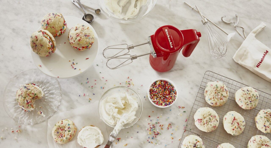 KitchenAid® hand mixer on countertop with frosting and sprinkles for homemade cupcakes. KitchenAid® hand mixer on countertop with frosting and sprinkles for homemade cupcakes.