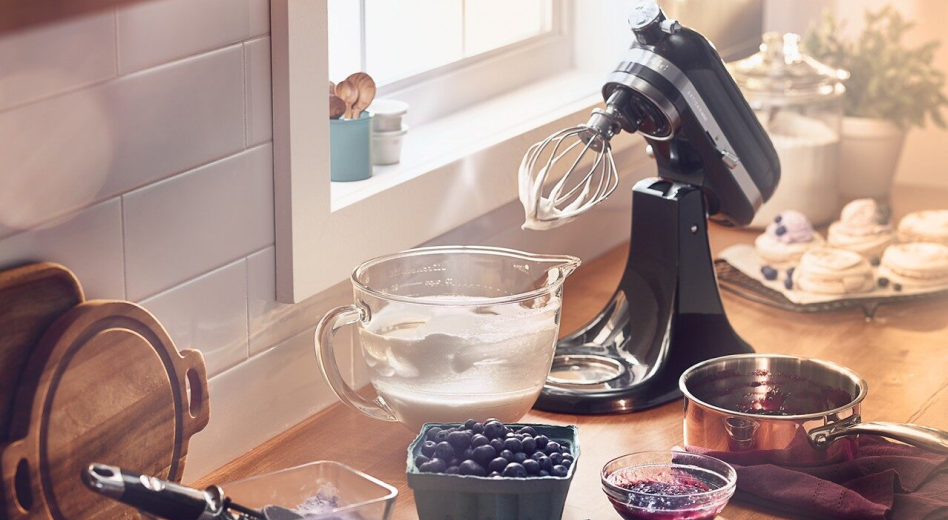 KitchenAid® stand mixer on countertop with whipped cream in a glass mixer bowl next to fresh berries. KitchenAid® stand mixer on countertop with whipped cream in a glass mixer bowl next to fresh berries.