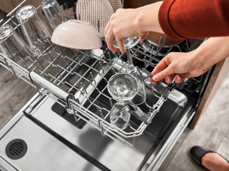 Person loading glassware into the top rack of a dishwasher