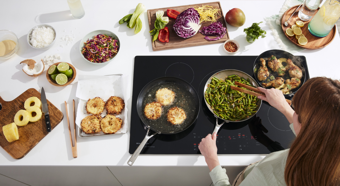 Person sauteeing green beans on electric cooktop surrounded by ingredients Person sauteeing green beans on electric cooktop surrounded by ingredients