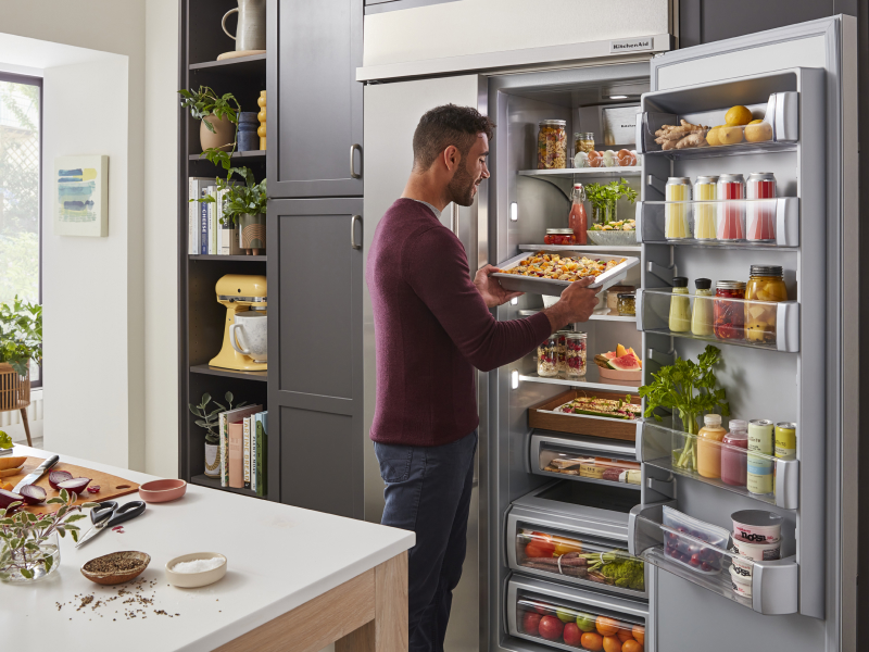 Person putting prepared baked goods in the refrigerator on a cookie sheet Person putting prepared baked goods in the refrigerator on a cookie sheet