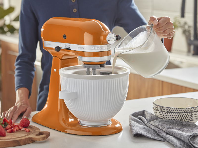 Person pouring milk into the white bowl of an orange stand mixer Person pouring milk into the white bowl of an orange stand mixer