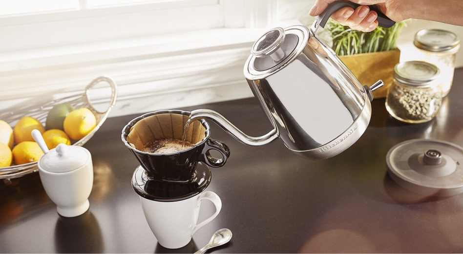 Hand pouring water from a gooseneck kettle over a pour over coffee cone Hand pouring water from a gooseneck kettle over a pour over coffee cone