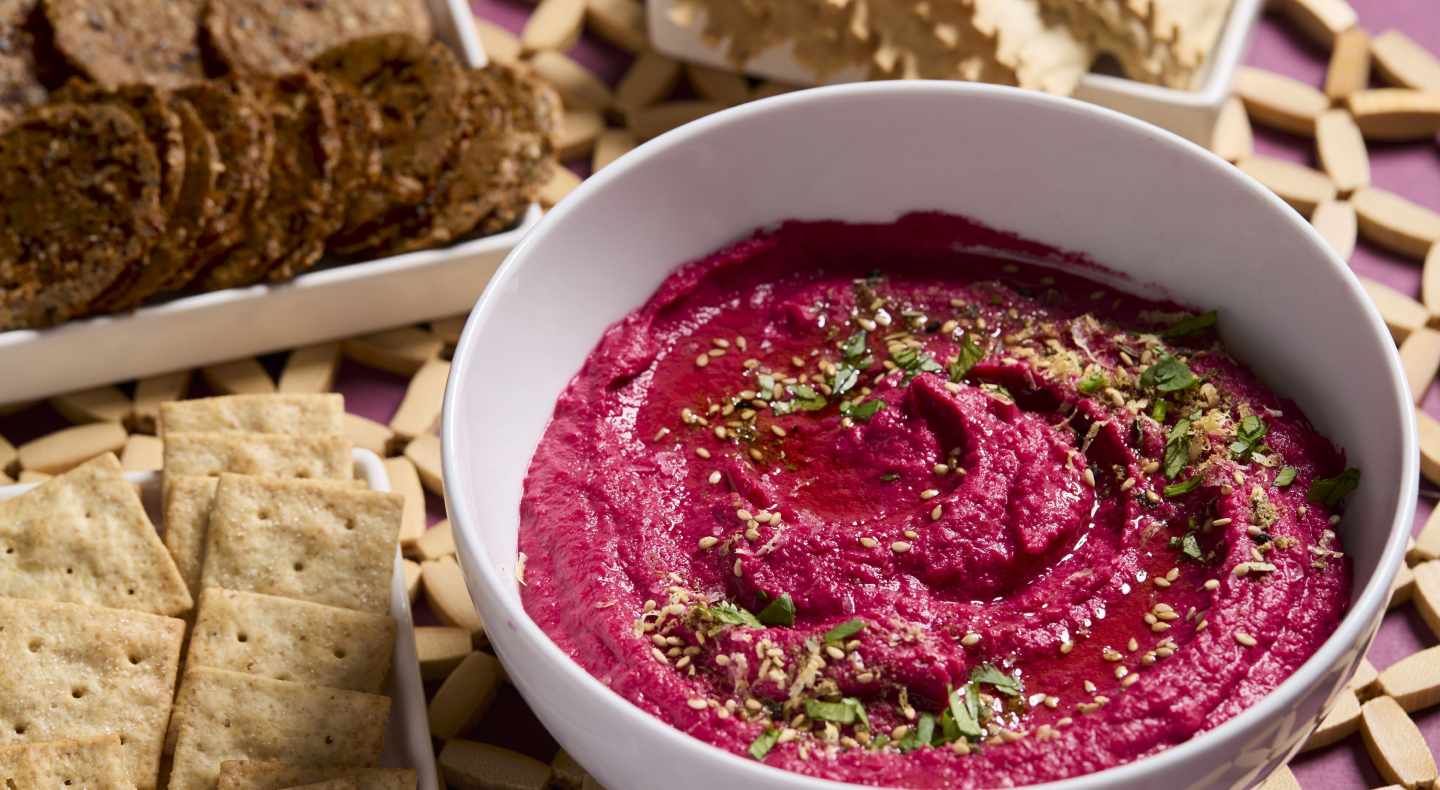 Beet hummus topped with herbs in a white bowl Beet hummus topped with herbs in a white bowl