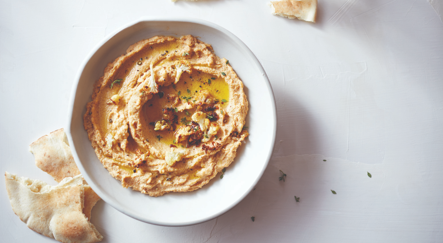 Hummus topped with herbs next to slices of pita bread Hummus topped with herbs next to slices of pita bread