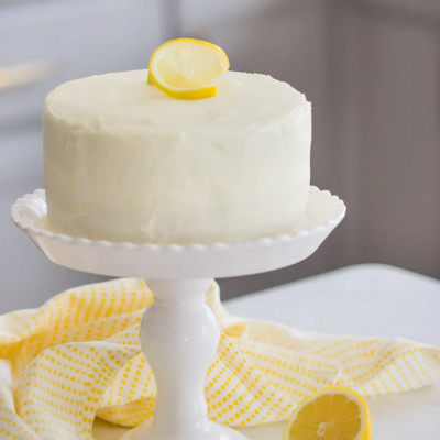 White frosted cake on top of cake stand topped with sliced lemon