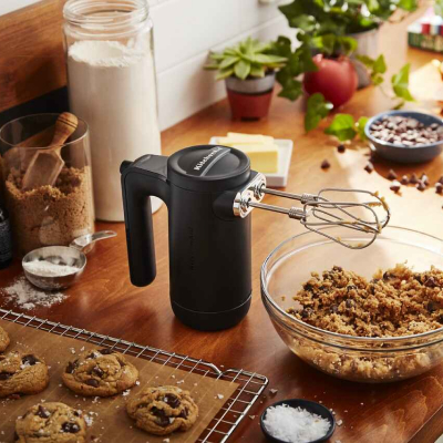 Black KitchenAid® hand mixer above bowl of cookie dough next to pan of baked cookies