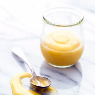 Mango curd in glass dish next to spoon on countertop