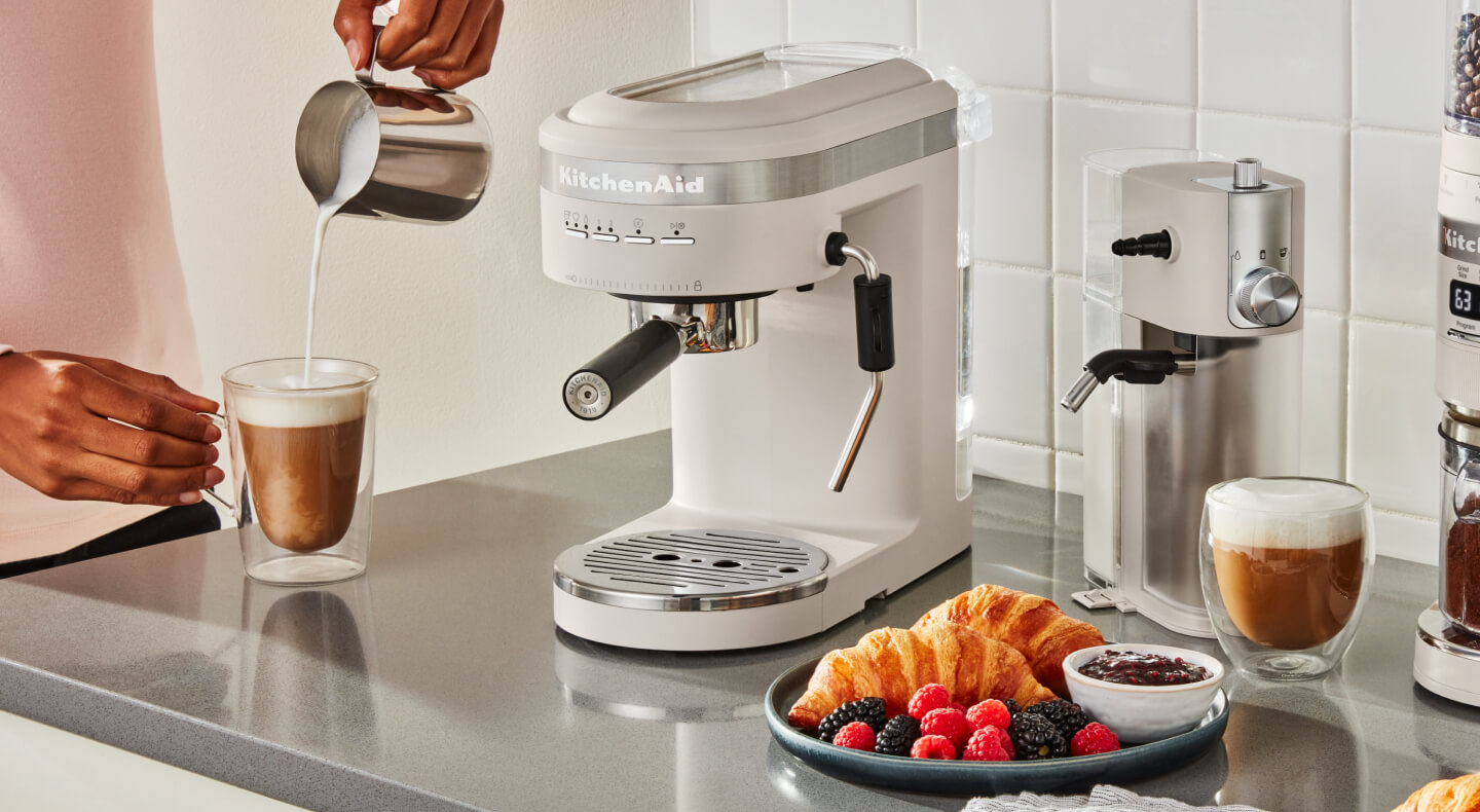 Person pouring frothed milk into an espresso drink next to an semi-automatic type of espresso machine Person pouring frothed milk into an espresso drink next to an semi-automatic type of espresso machine