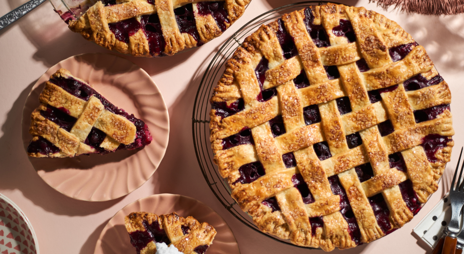 A homemade blueberry pie sittlng next to a couple of plates of slices of the pie. A homemade blueberry pie sittlng next to a couple of plates of slices of the pie.