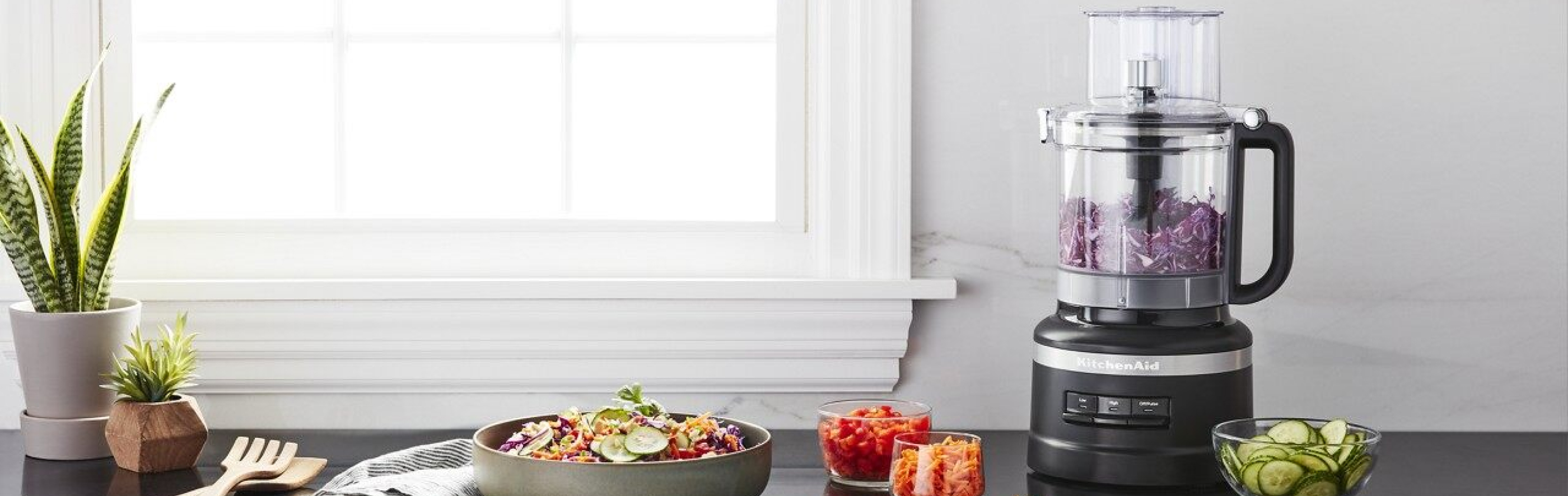 Black KitchenAid® food processor with shredded cabbage next to a salad