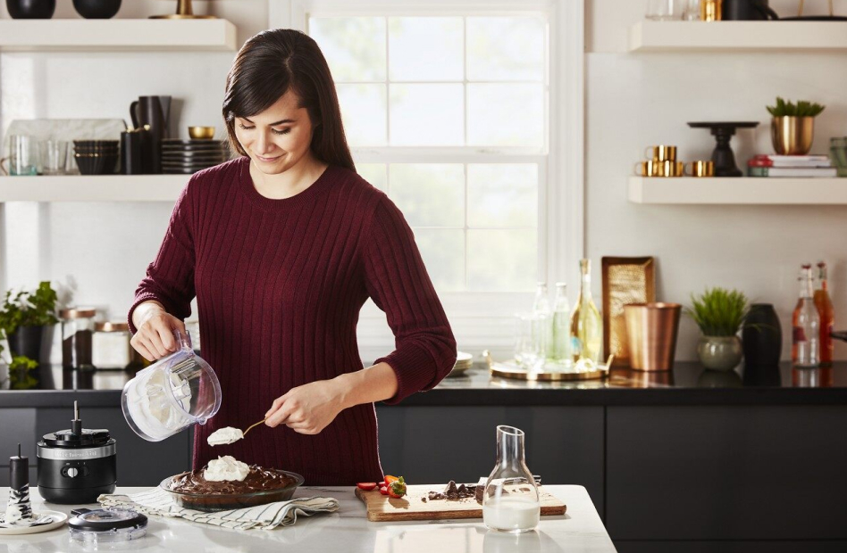 Woman spooning whipped cream from a cordless food chopper onto a chocolate pie Woman spooning whipped cream from a cordless food chopper onto a chocolate pie